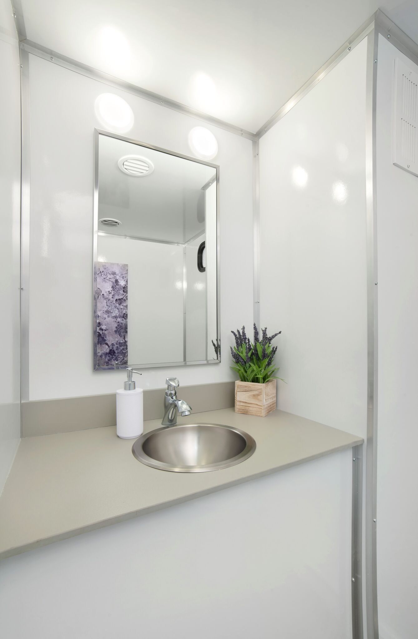 Portable restroom trailer sink area with mirror and soap dispenser.