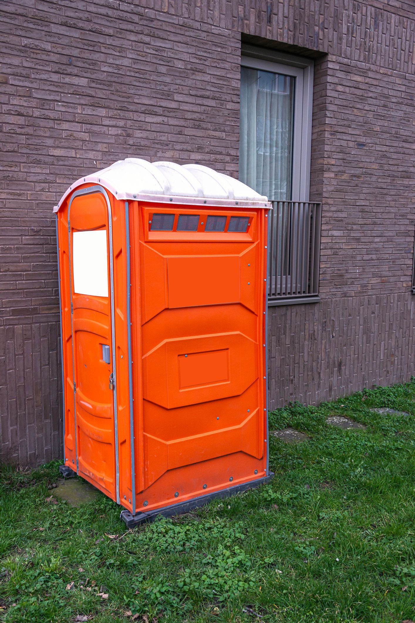 Mobile outdoor toilet cabin placed on grass near an apartment for portable toilet rental service.