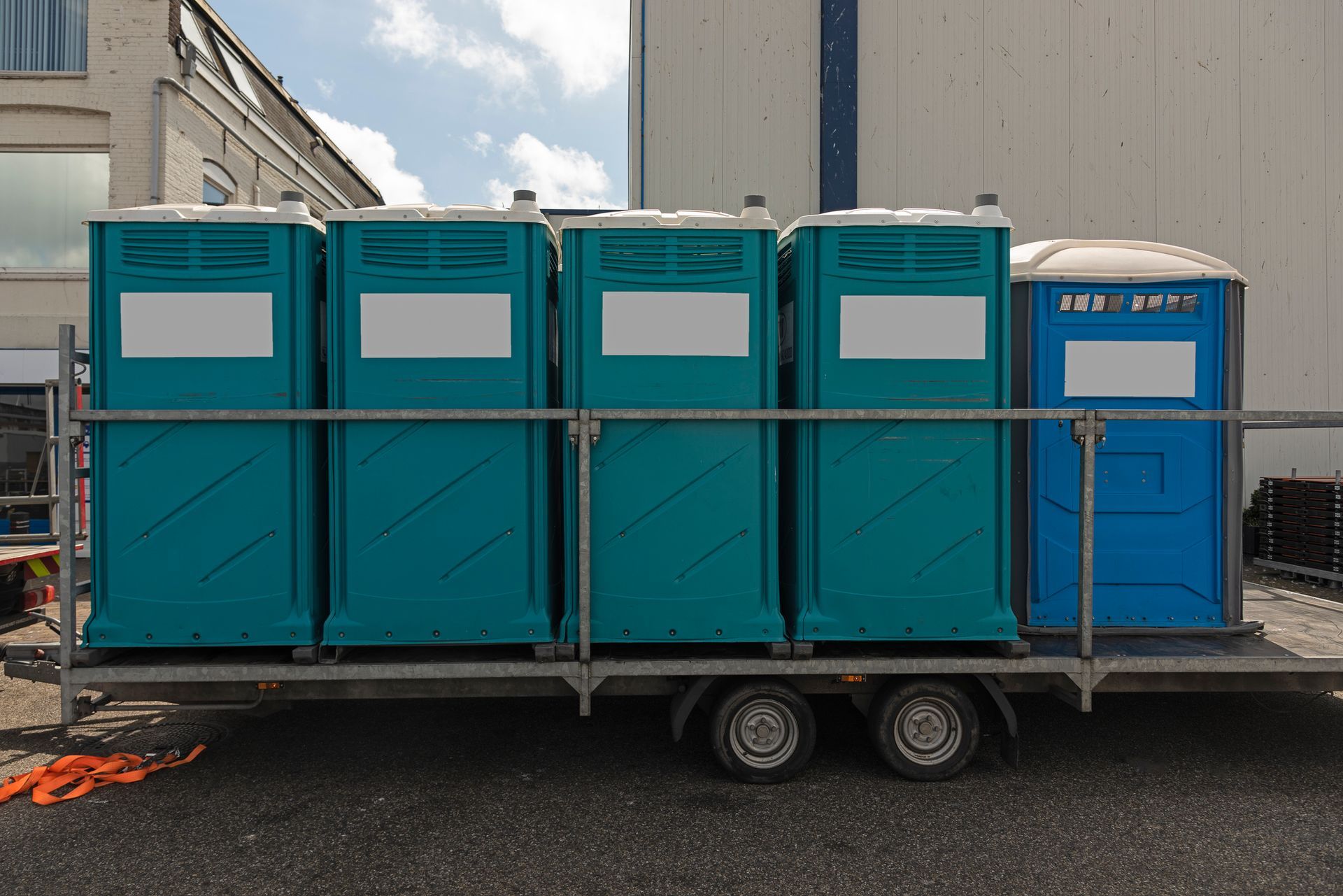 Some aqua-colored mobile toilets are lined up outside on a trailer.