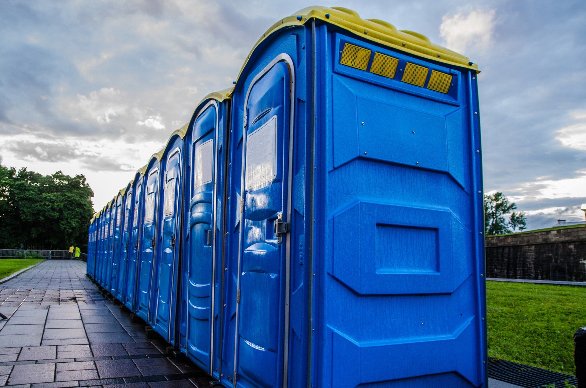 A row of blue portable toilets are lined up in a park. A row of blue portable toilets are lined up in a park.