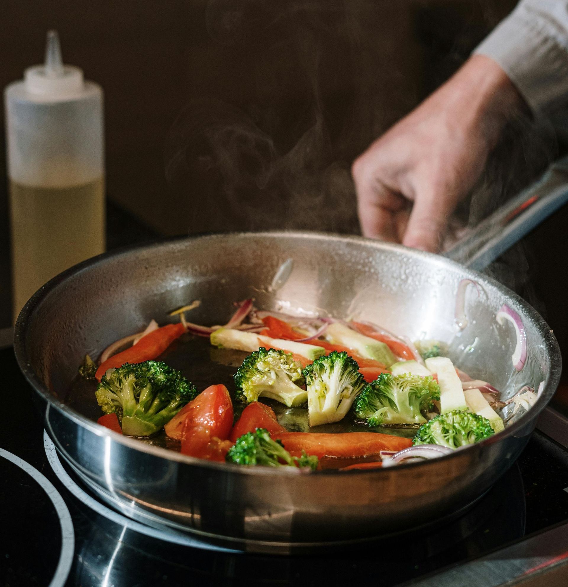 A person is cooking vegetables in a frying pan on a stove.