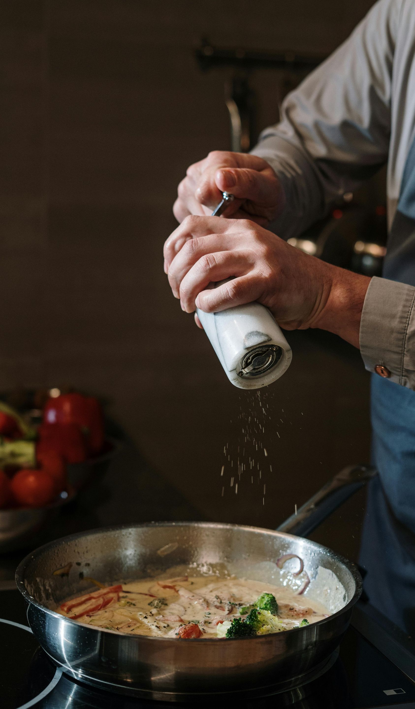 A person is adding salt to a pan of food.