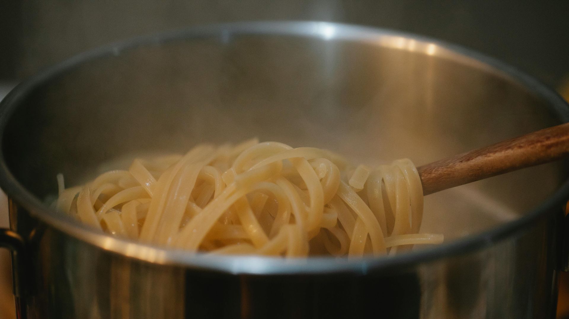 Spaghetti is being cooked in a pot with a wooden spoon.