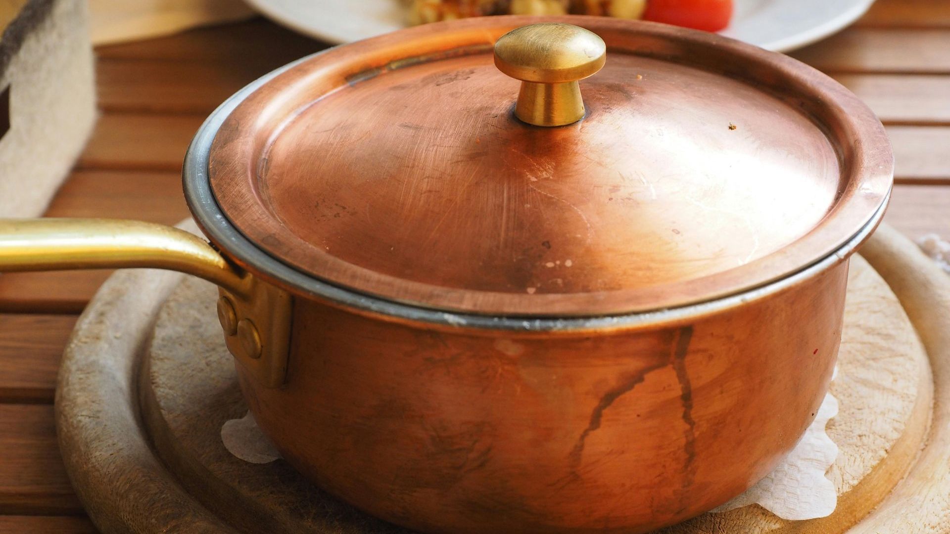 A copper pot with a lid is sitting on a wooden table.