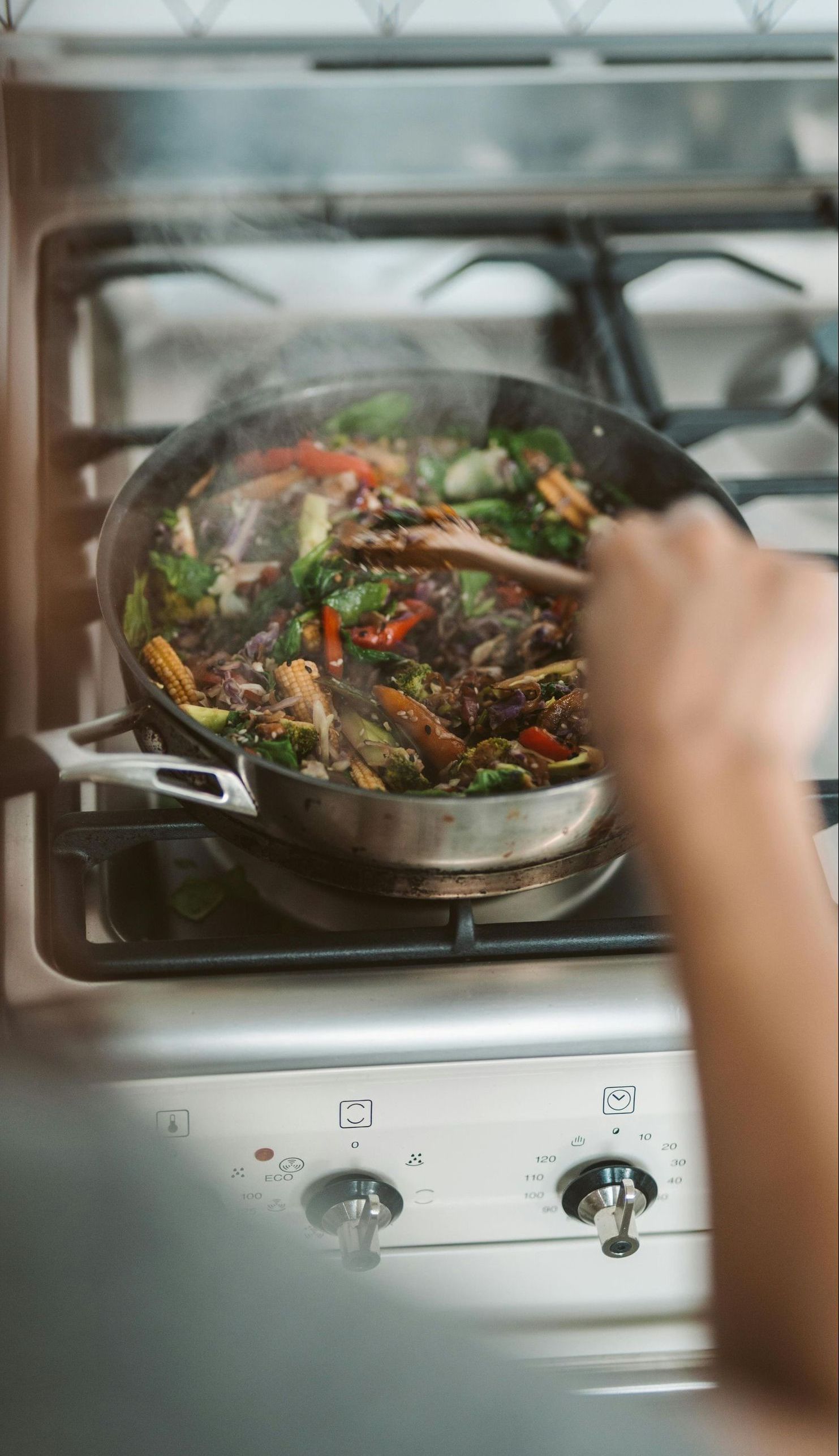 A person is cooking vegetables in a pan on a stove.