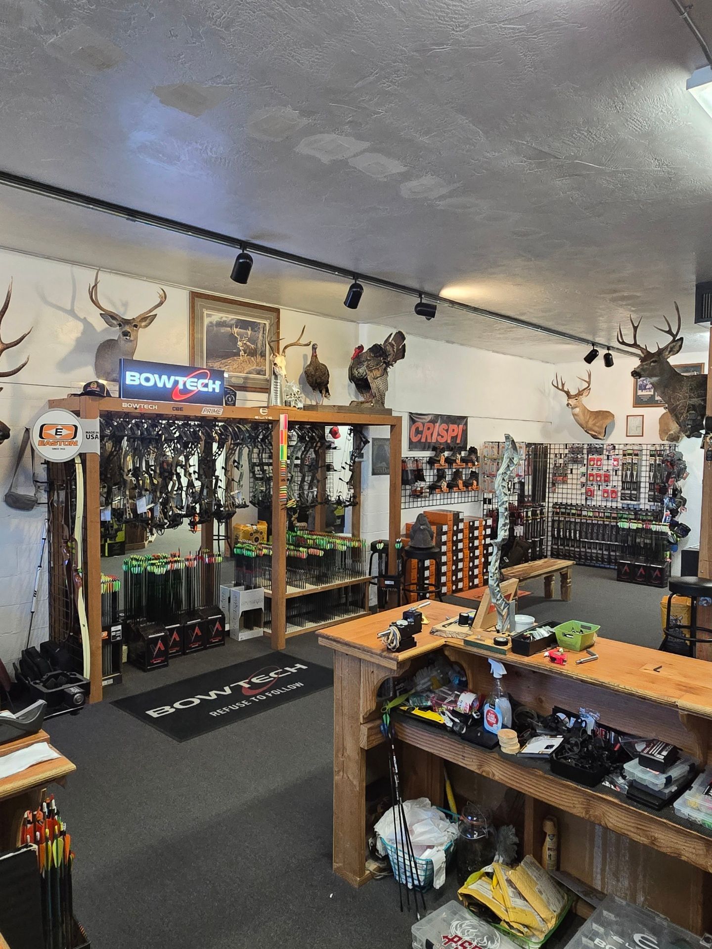 Hunting gear shop interior with rows of rifles, bows, and mounted deer heads on the walls.