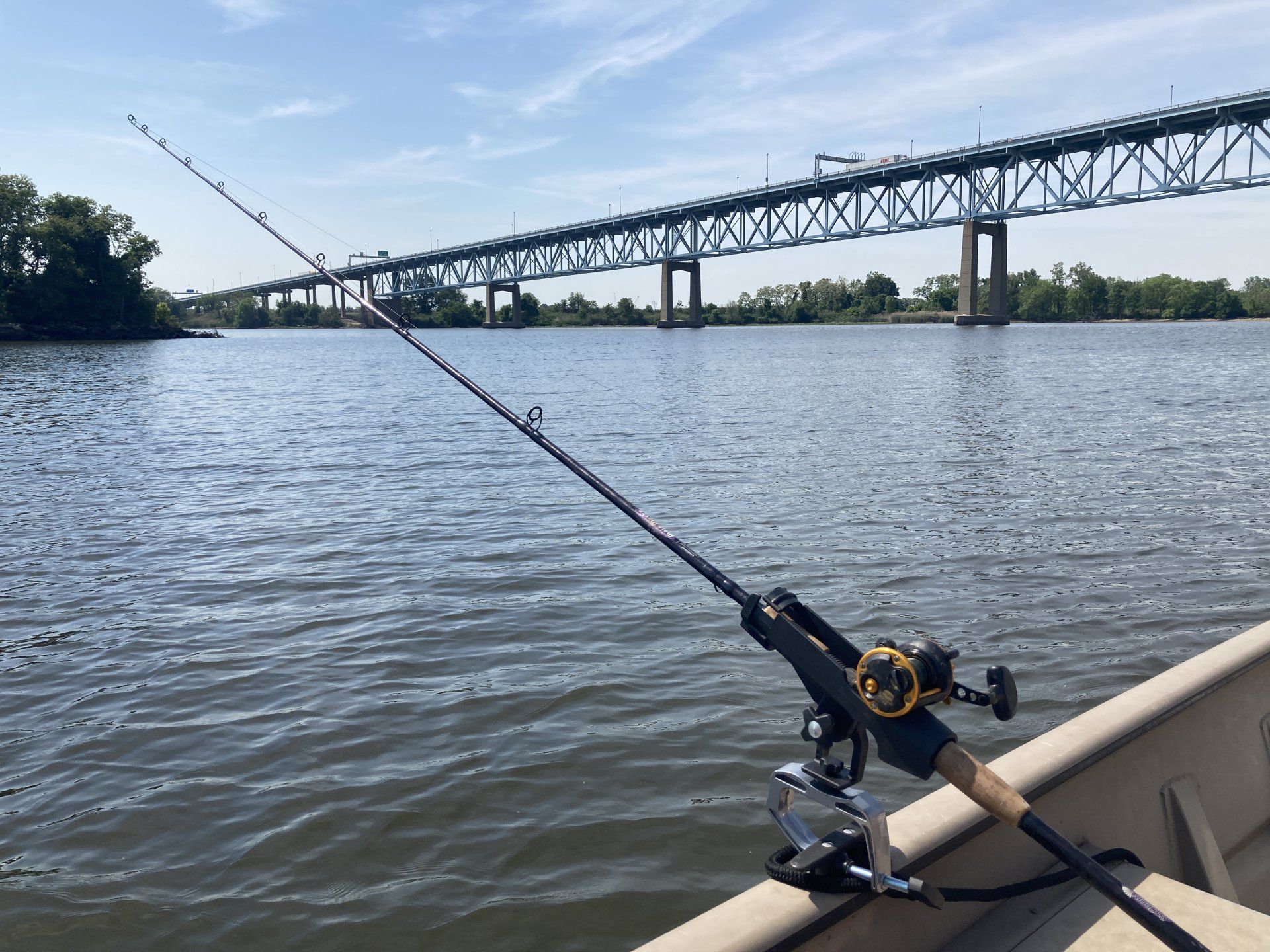 A fishing rod is shown attached to a boat in the Delaware River with a bridge view in the background.