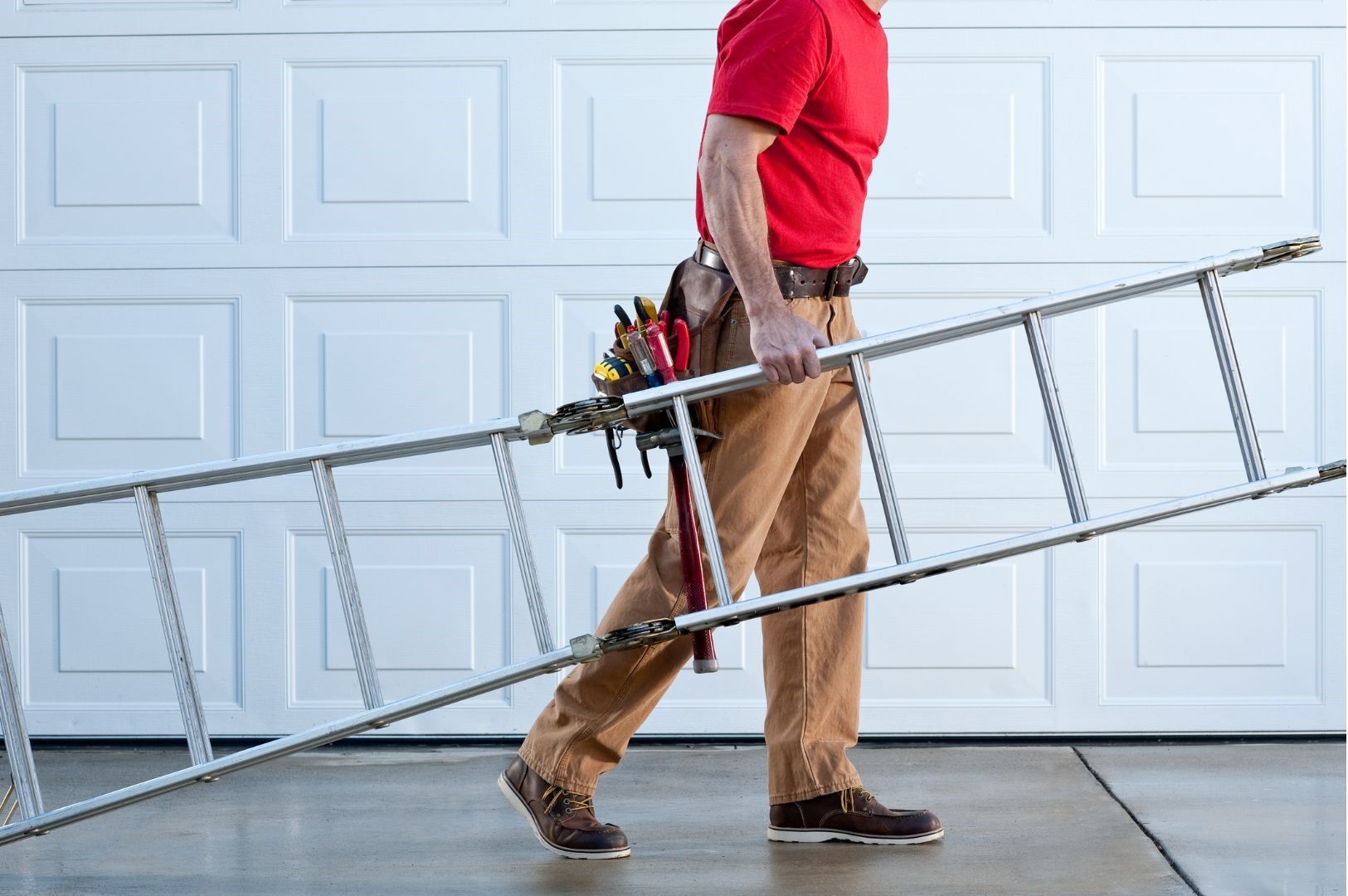 A man is carrying a ladder in front of a garage door.