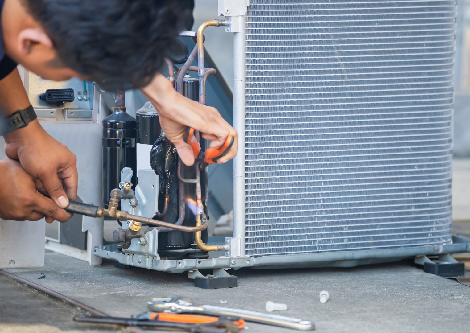 A man is working on an air conditioner with a wrench.