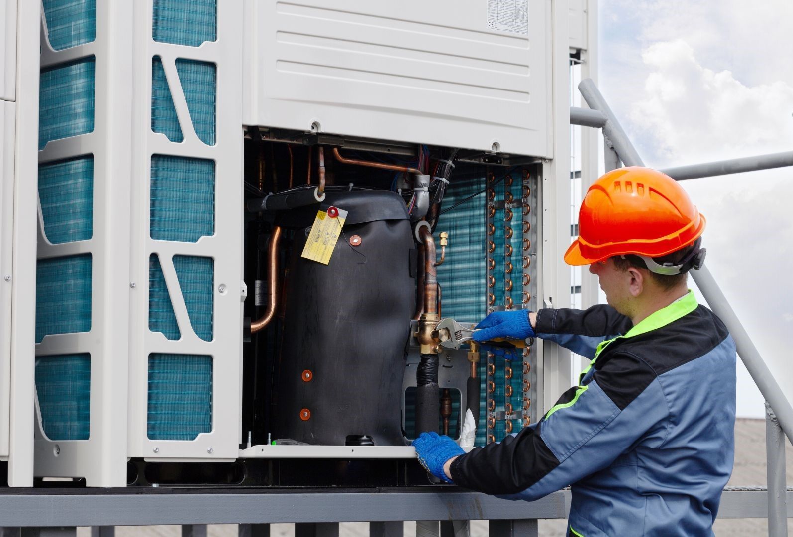 A man wearing a hard hat is working on an air conditioner.