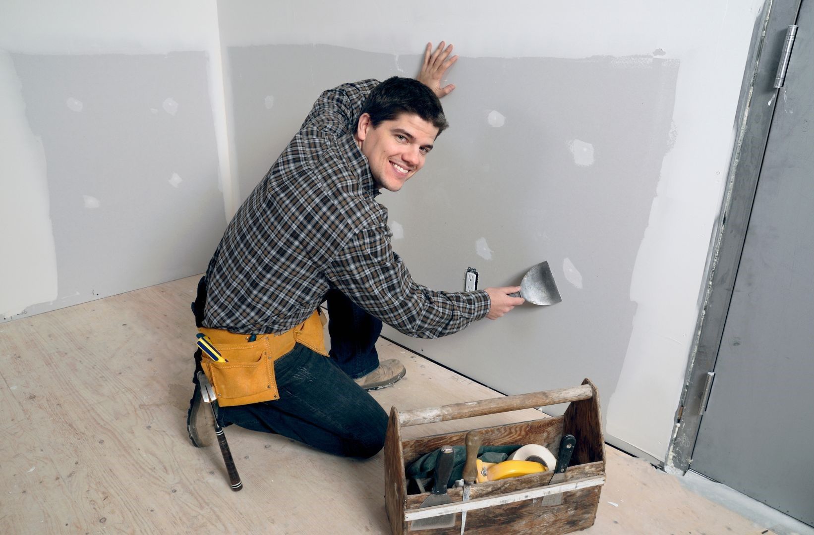 A man is kneeling down while using a spatula on a wall.