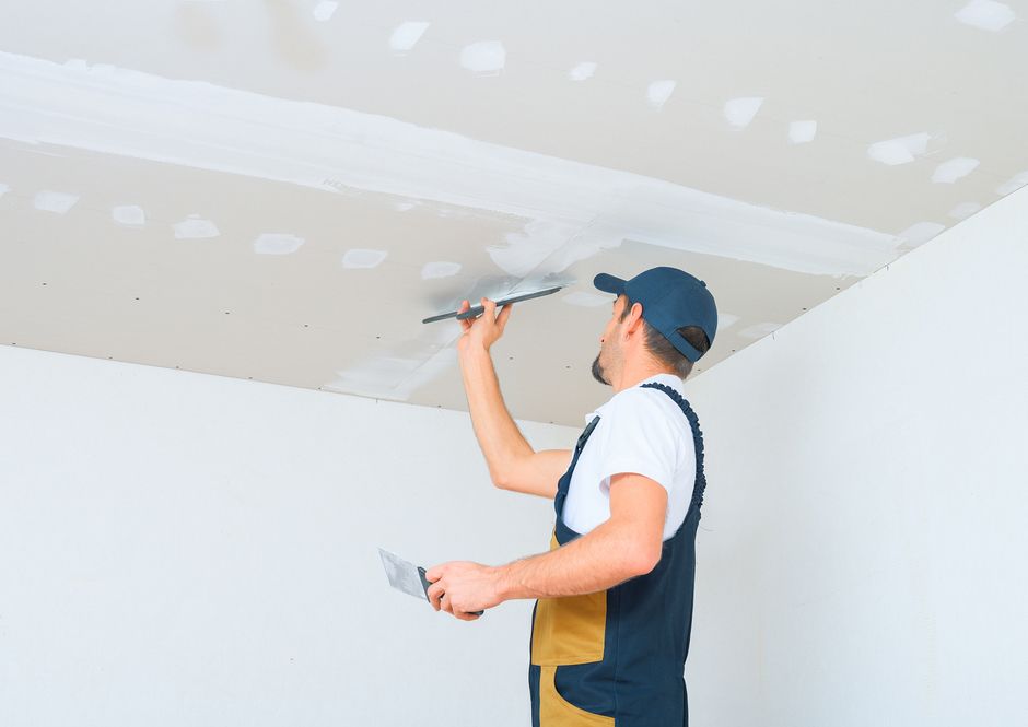 A man is plastering a ceiling with a spatula.