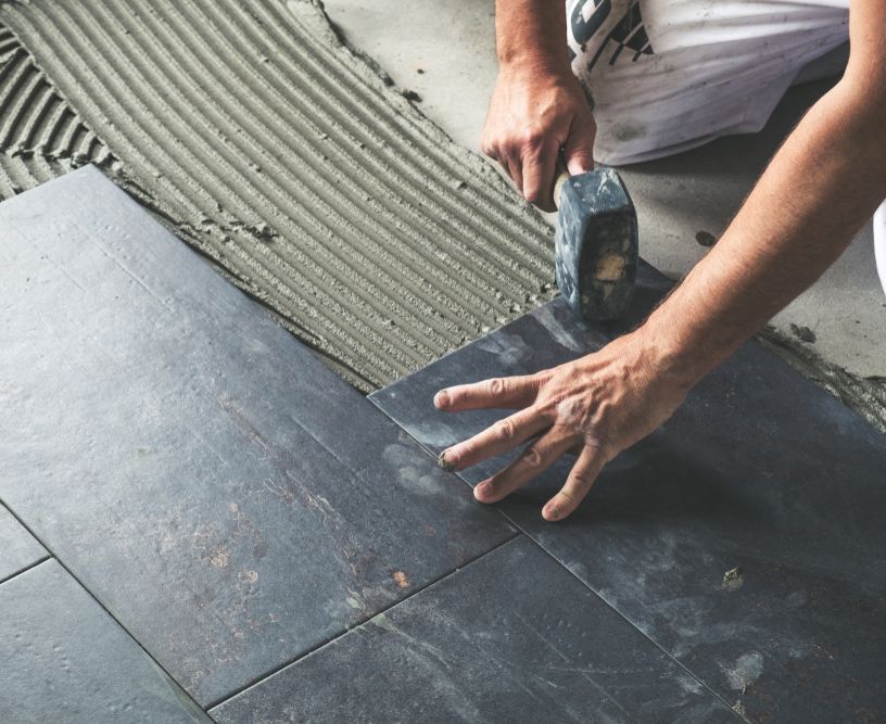 A man is laying tiles on the floor with a hammer.