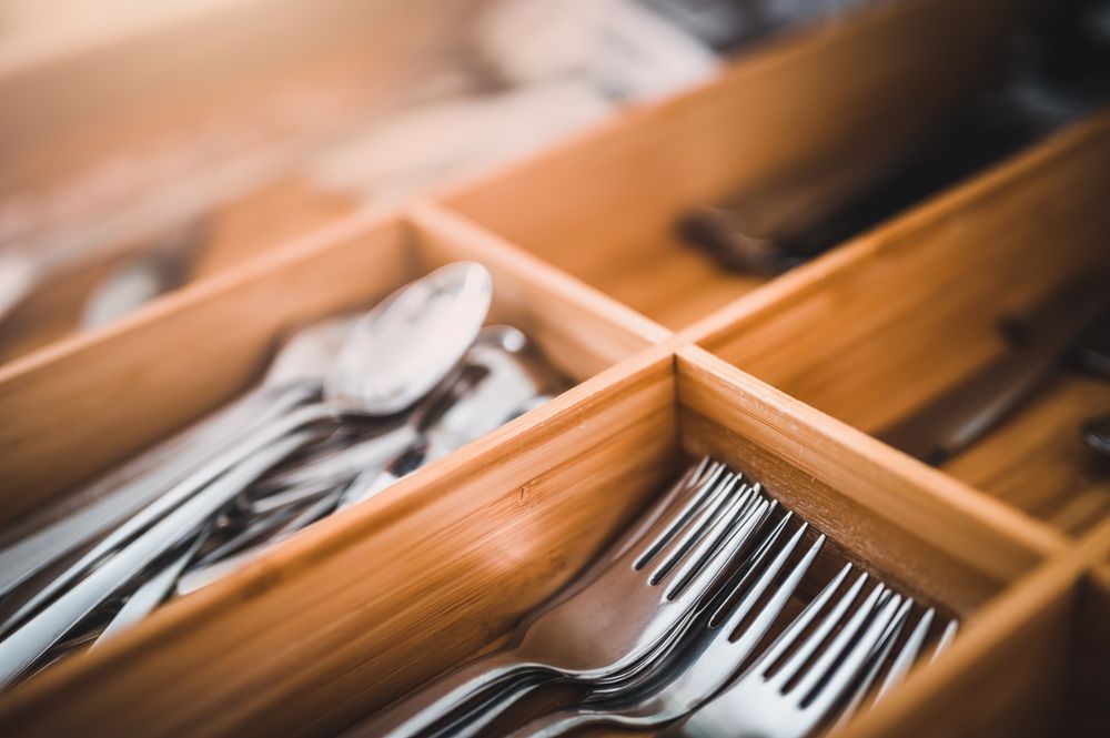 A wooden drawer filled with silverware including forks and spoons.