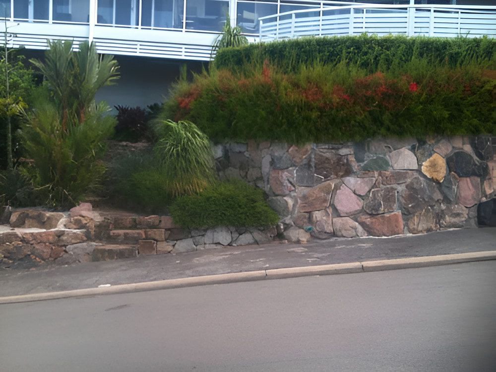 A Stone Wall Is Surrounded By Trees And Bushes — Baker & Co. Landscape Construction In Gulliver, QLD
