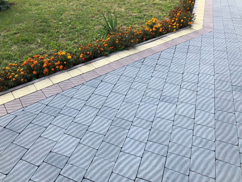 A Brick Driveway With Flowers On The Side Of It — Baker & Co. Landscape Construction In Gulliver, QLD