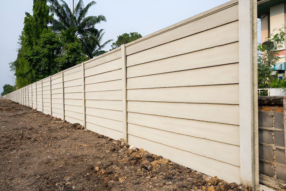 A Long White Concrete Fence Is Surrounded By Dirt And Trees — Baker & Co. Landscape Construction In Gulliver, QLD