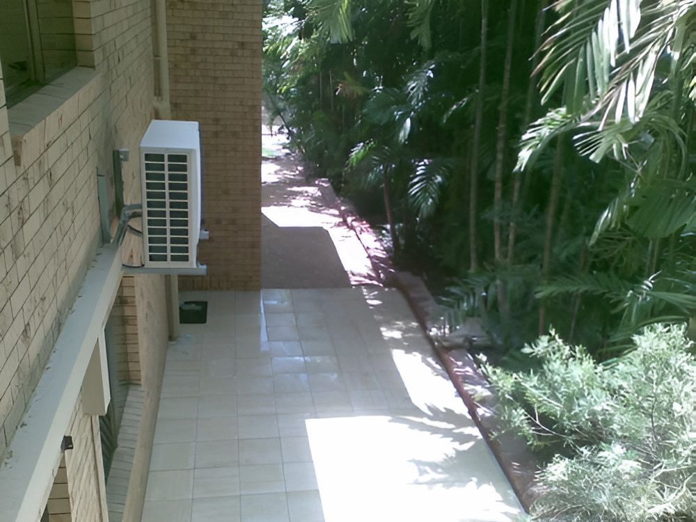 A White Air Conditioner Is Mounted On The Side Of A Building — Baker & Co. Landscape Construction In Gulliver, QLD