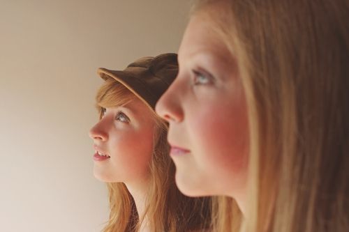 Two young girls are standing next to each other wearing hats.