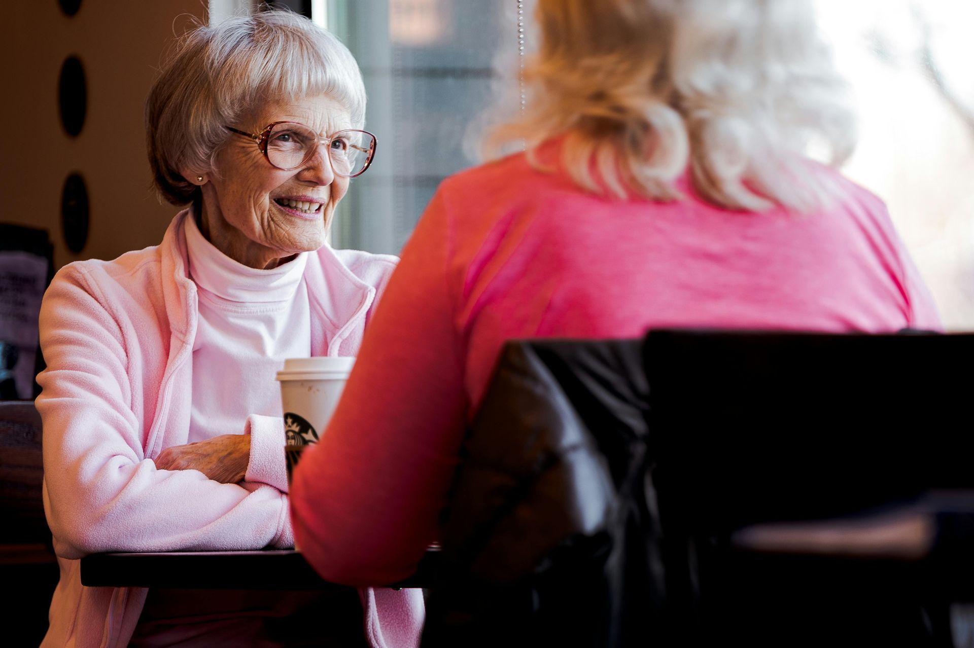 Two older women are sitting at a table drinking coffee.