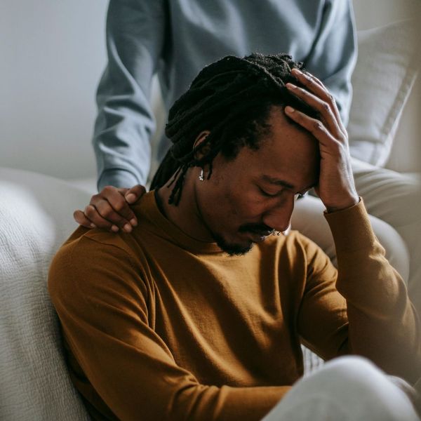 A man is sitting on a couch with his hand on his head.