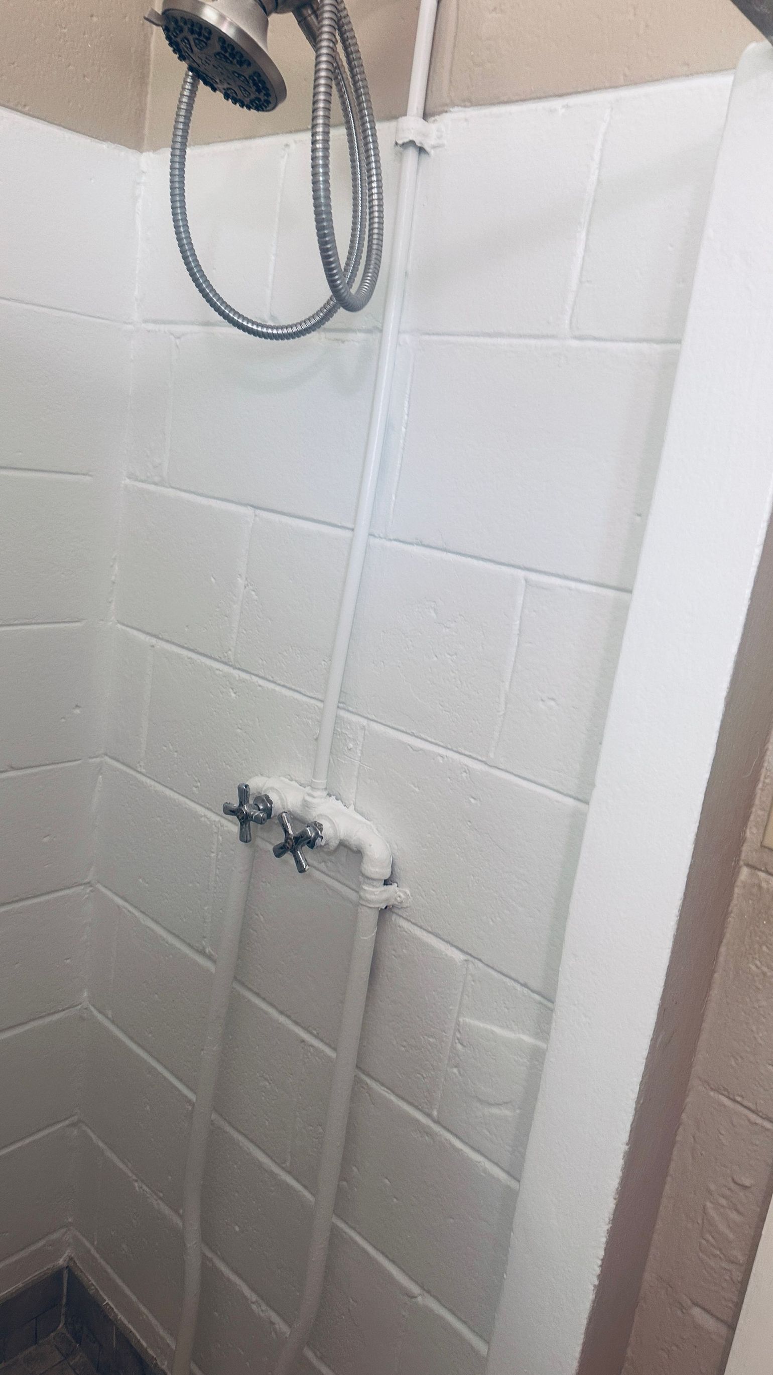 White tiled shower with a chrome showerhead and faucet, viewed from inside the stall.