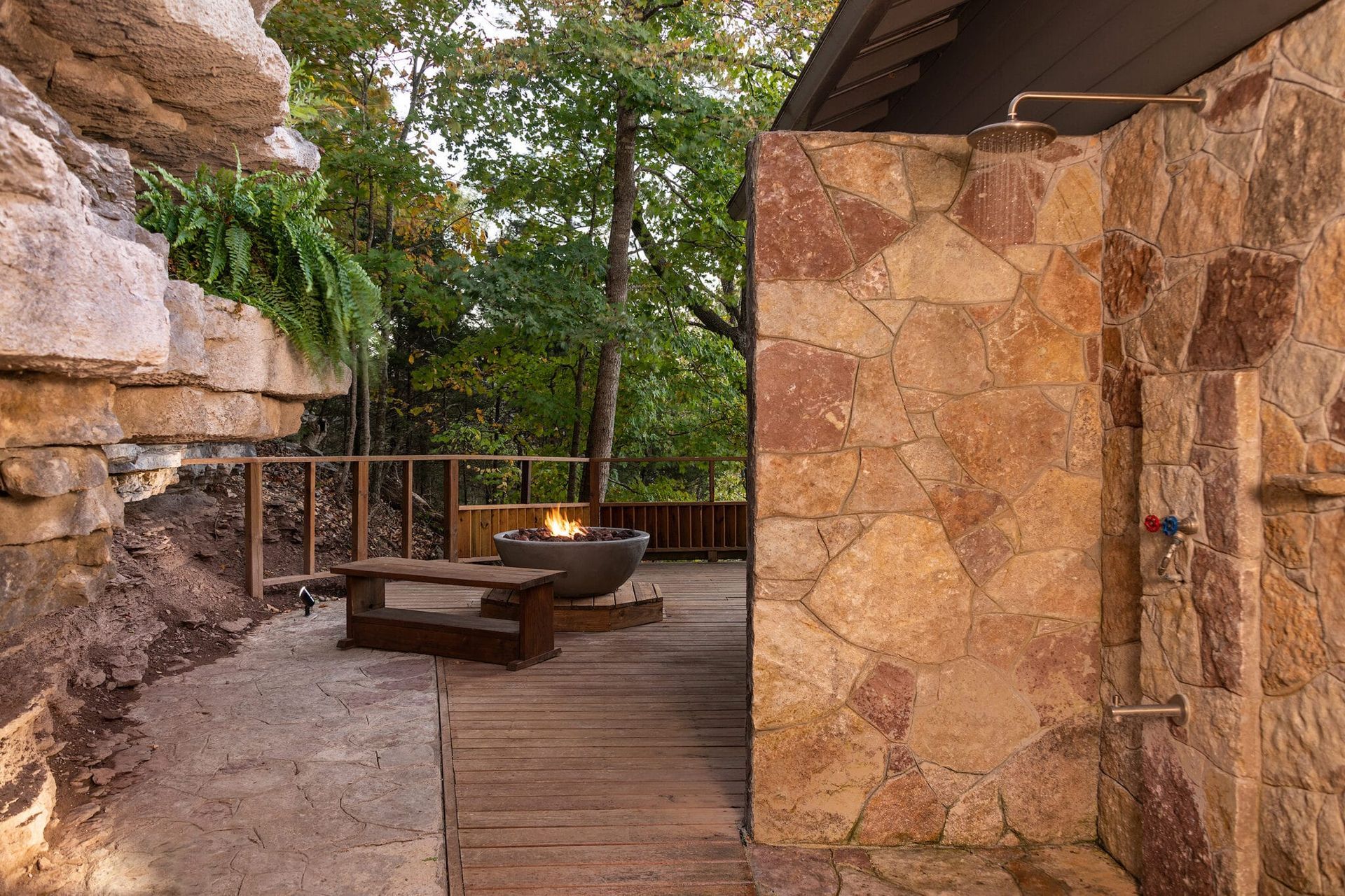 A stone wall with a shower and a fire pit in the background.