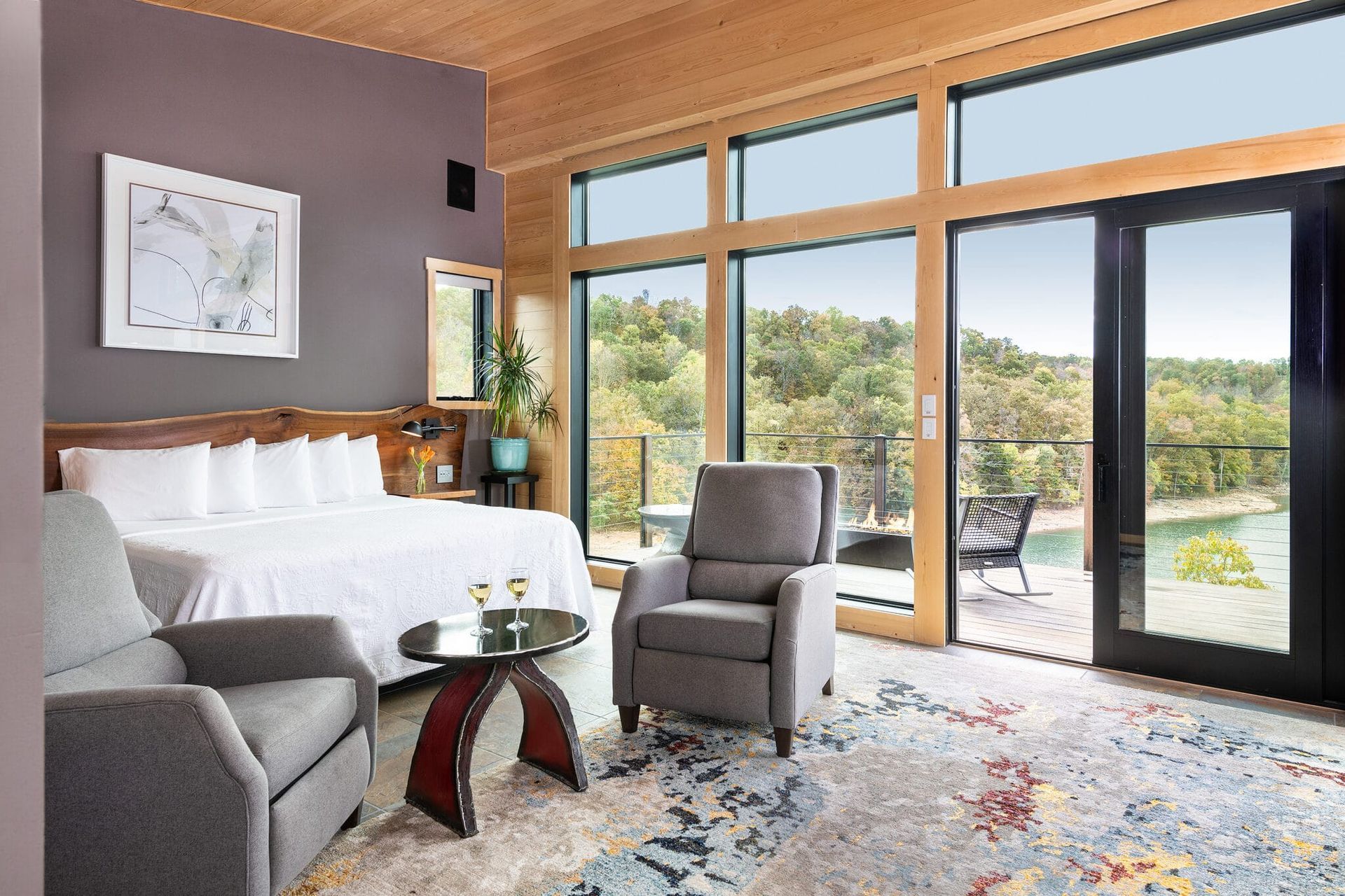 A bedroom with a king size bed , chair , table and sliding glass doors.