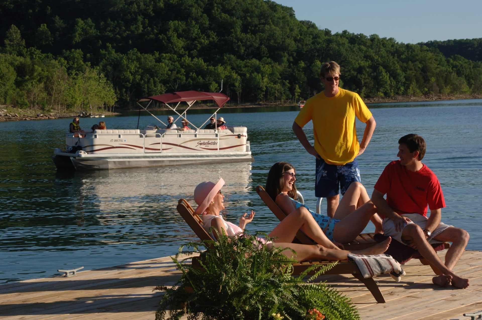 A group of people sitting on a dock with a boat in the background