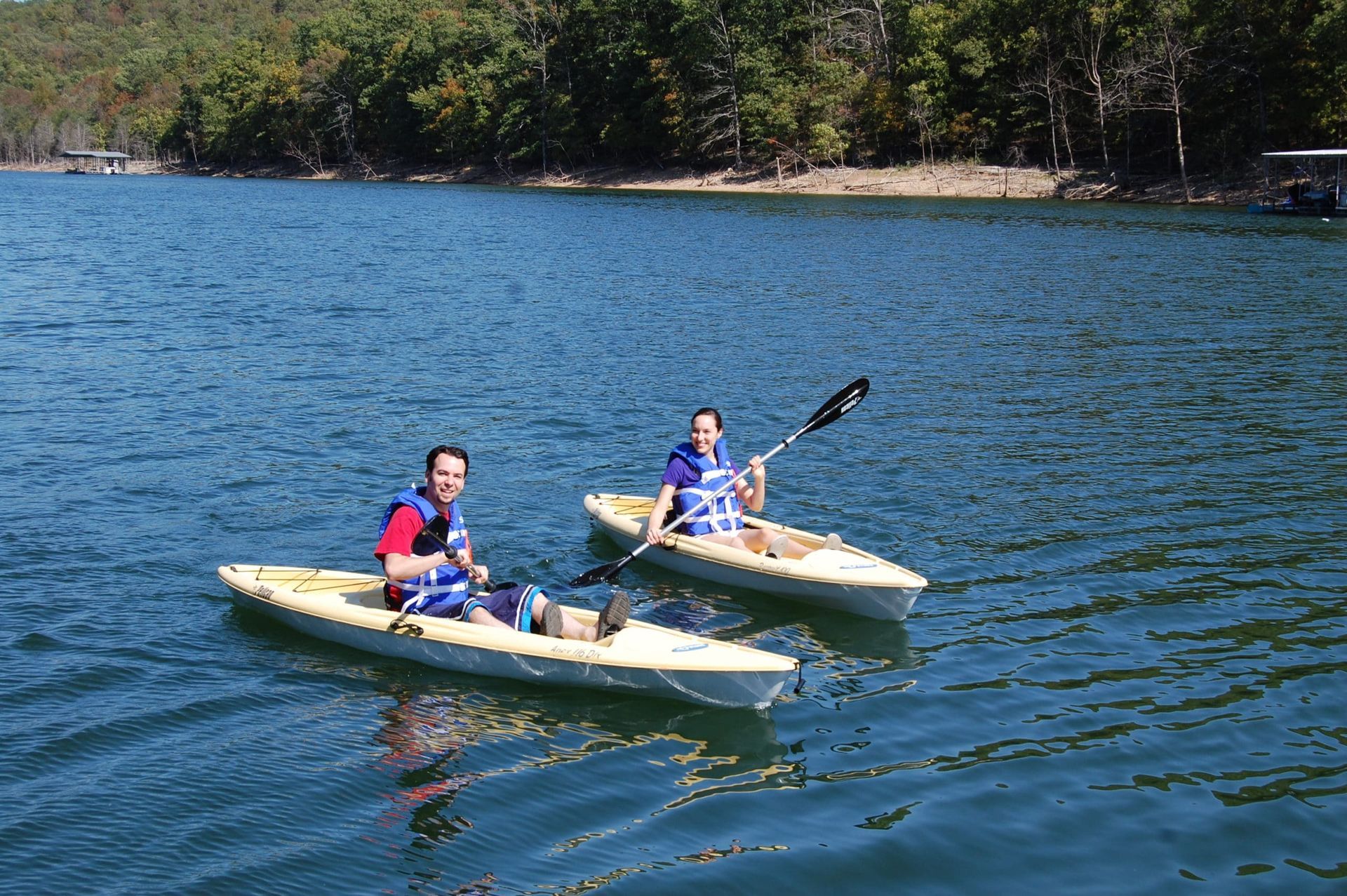 Two people are paddling kayaks on a lake.
