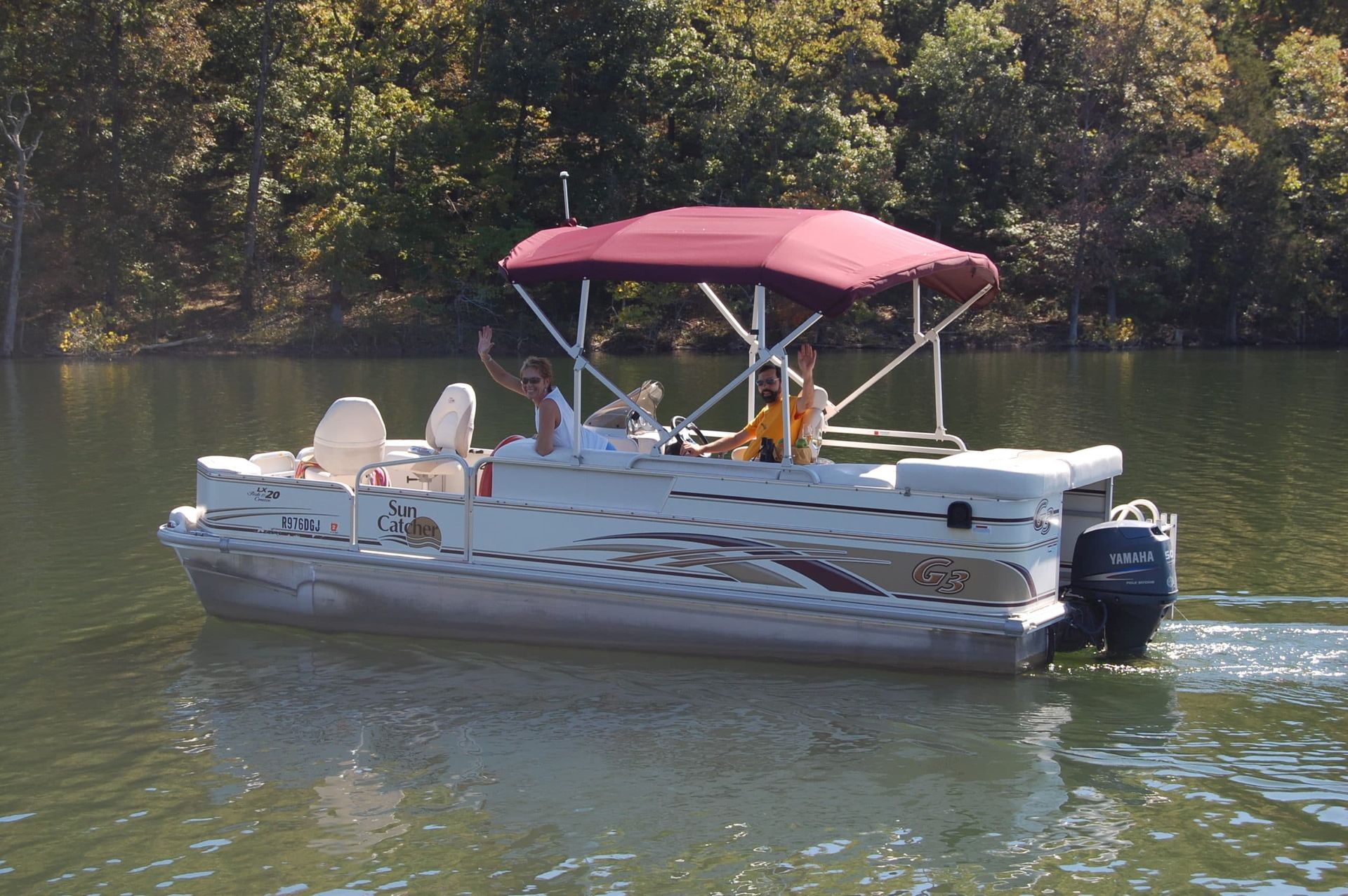 A pontoon boat with a red canopy is floating on a lake