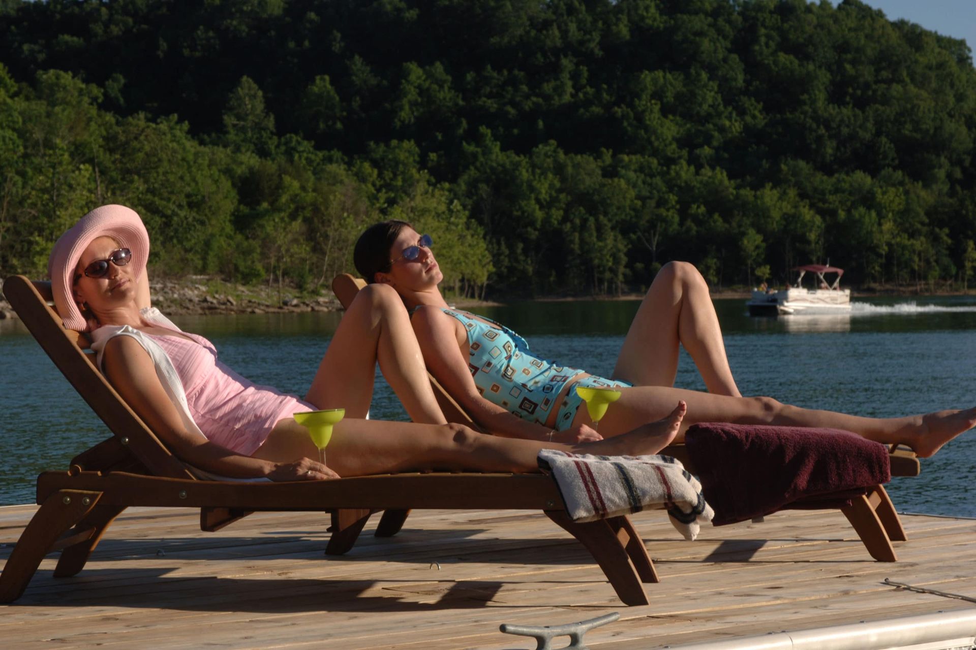 Three women are sunbathing on a dock with a boat in the background