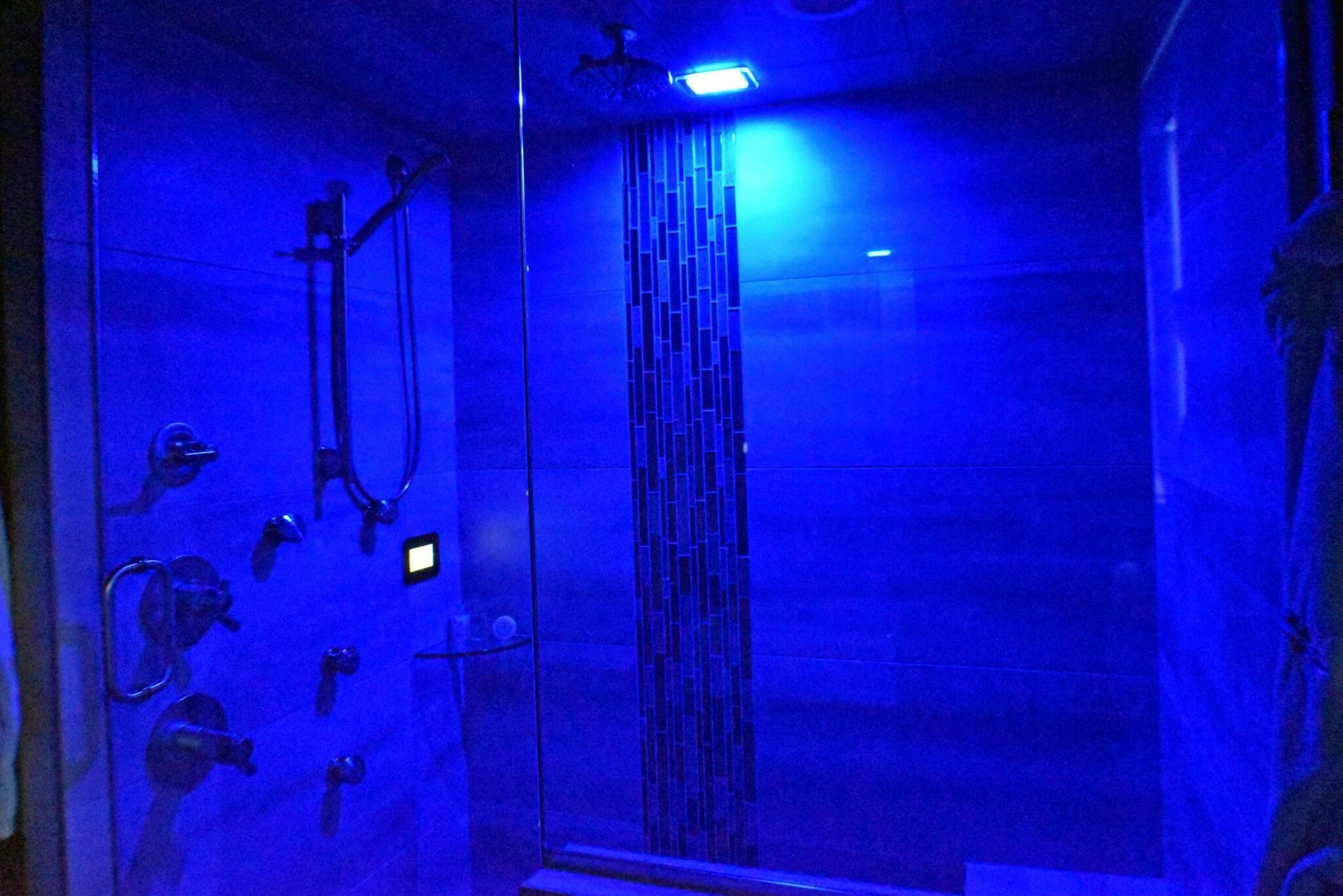 A shower with blue lights on the walls and ceiling.