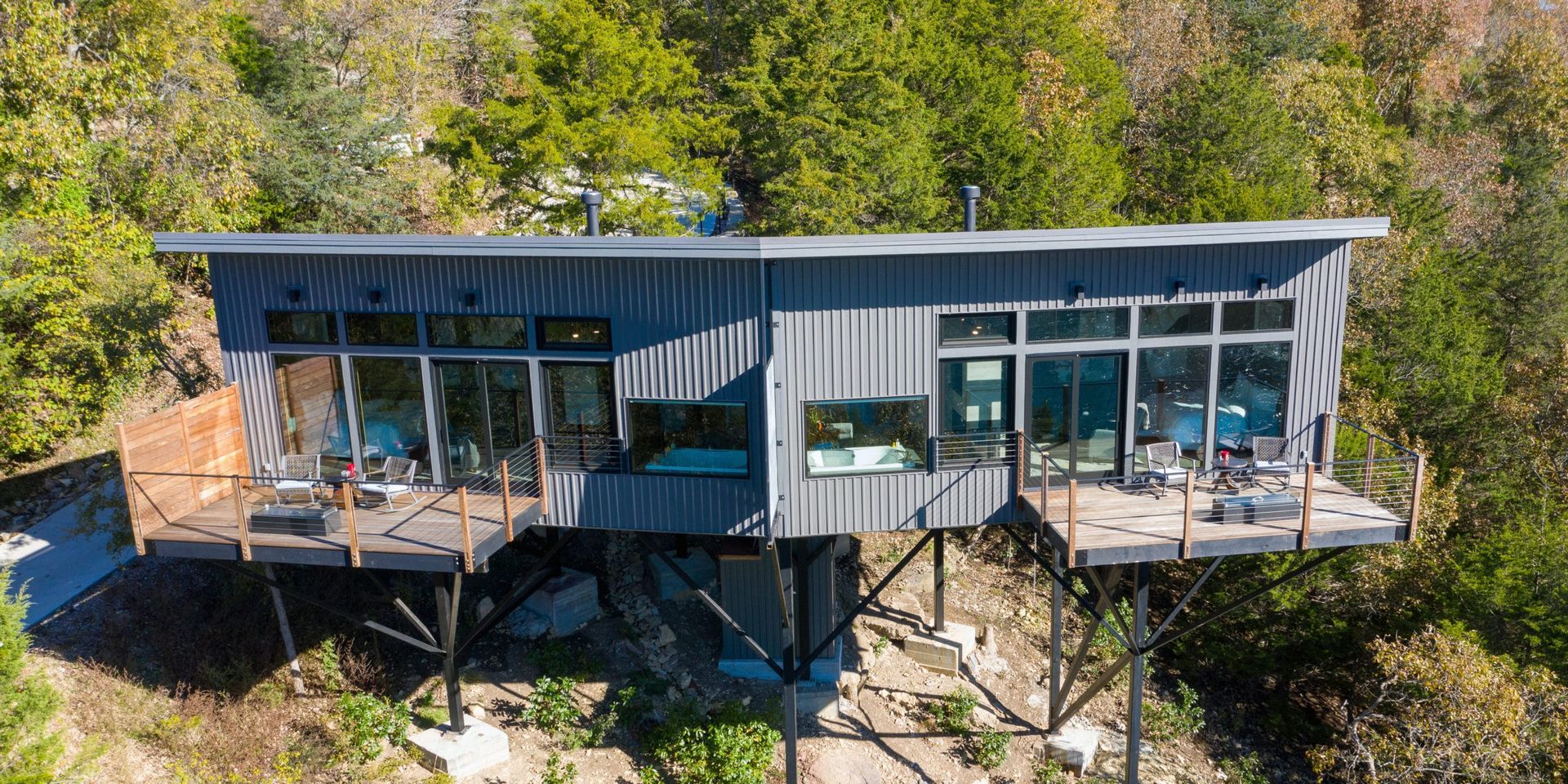 An aerial view of a modern house on stilts in the middle of a forest.