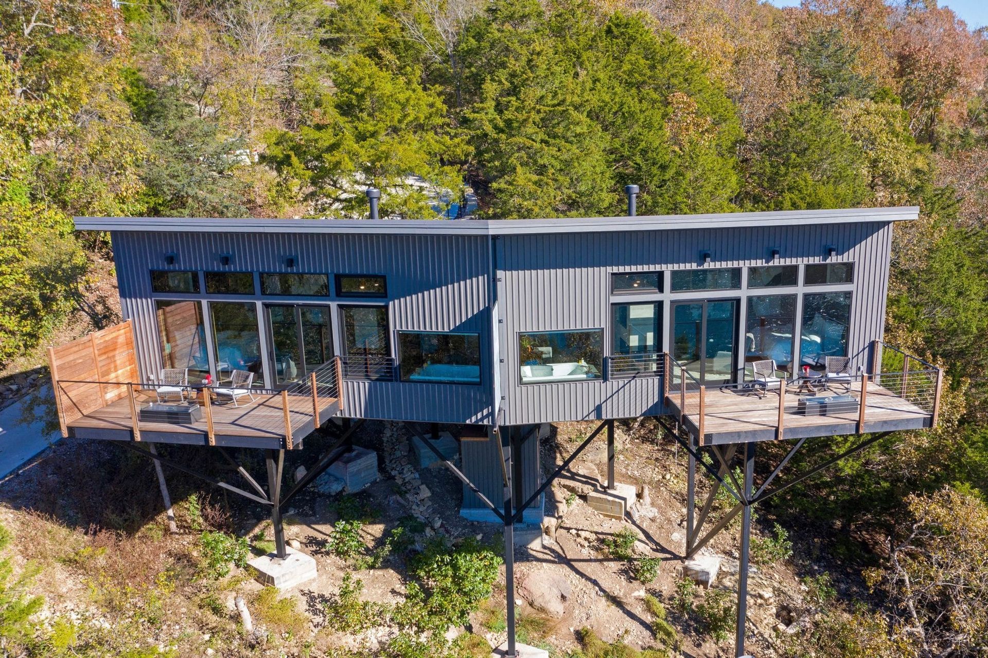 An aerial view of a modern house on stilts in the middle of a forest.