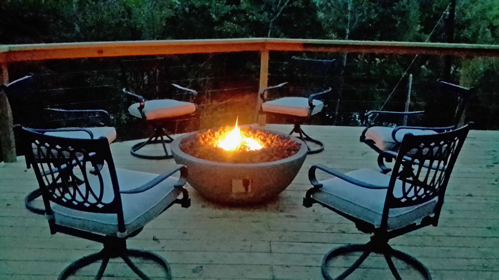 A fire pit is surrounded by chairs on a deck.