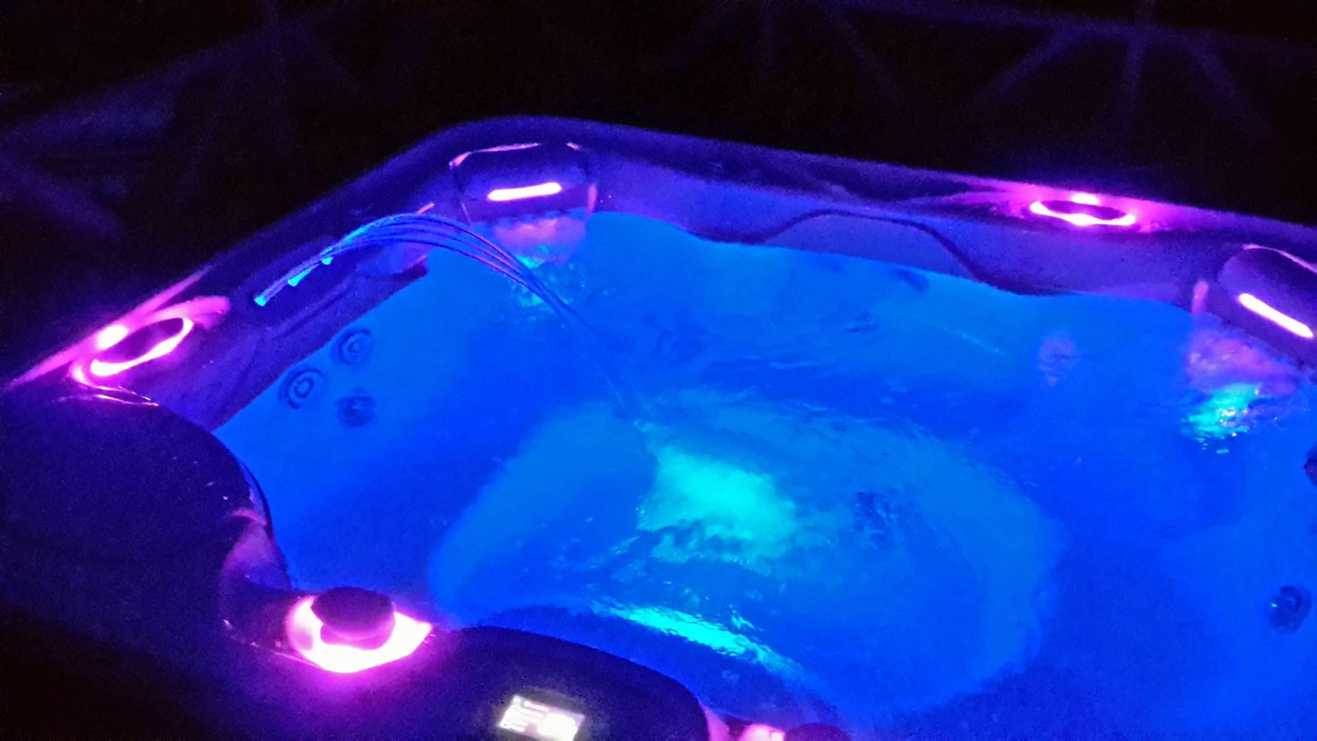 A hot tub is lit up with blue and purple lights at night.