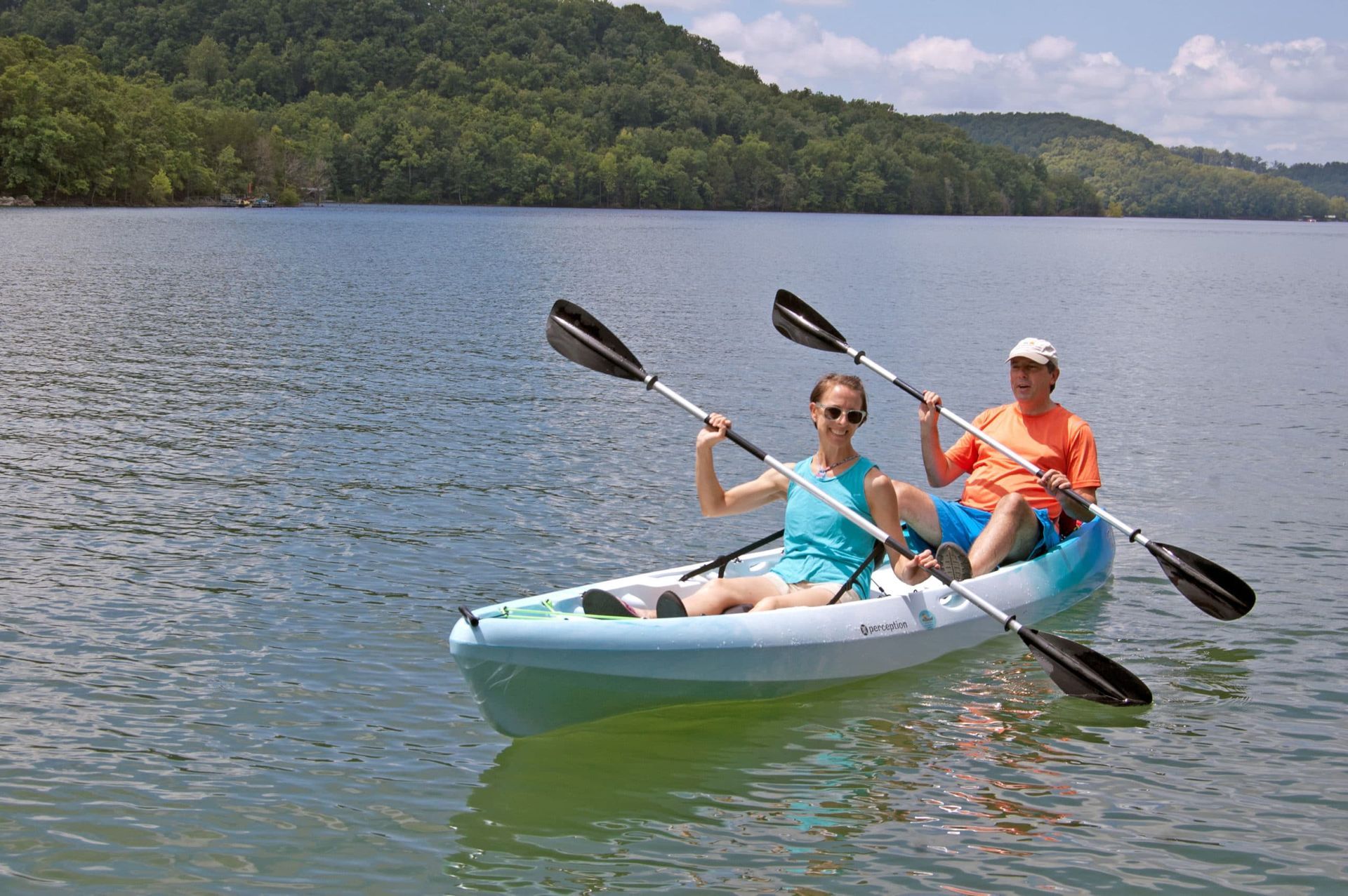 A man and a woman are paddling kayaks on a lake.