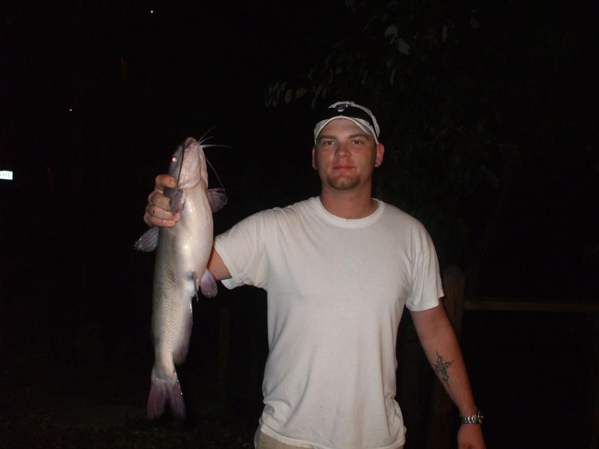 A man in a white shirt is holding a fish in his hand.