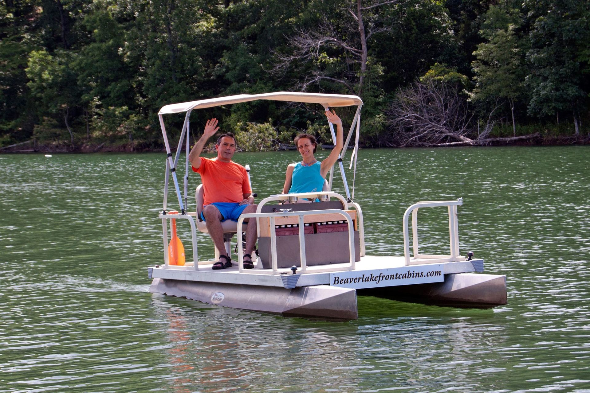 A man and a woman are riding a pontoon boat on a lake.