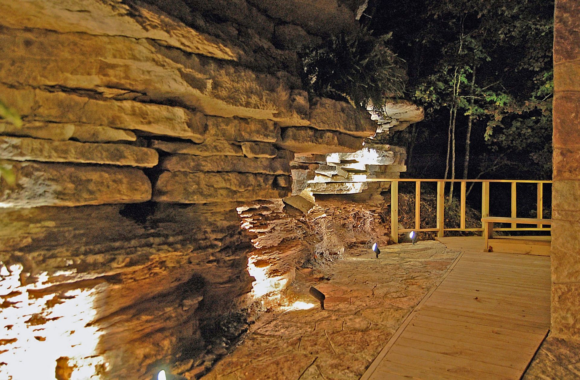 A stone wall is lit up at night with trees in the background