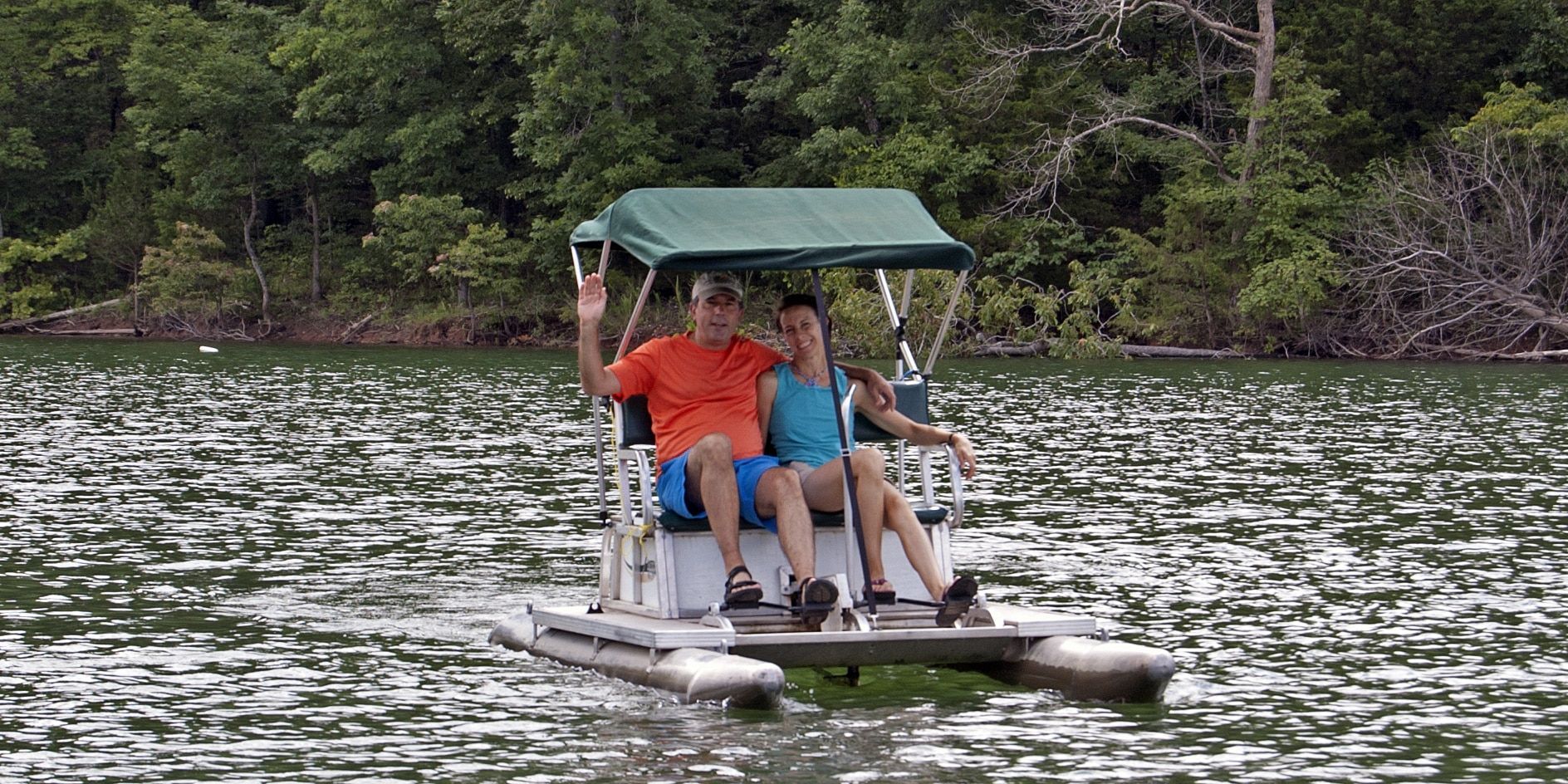 A man and a woman are riding a pedal boat on a lake.