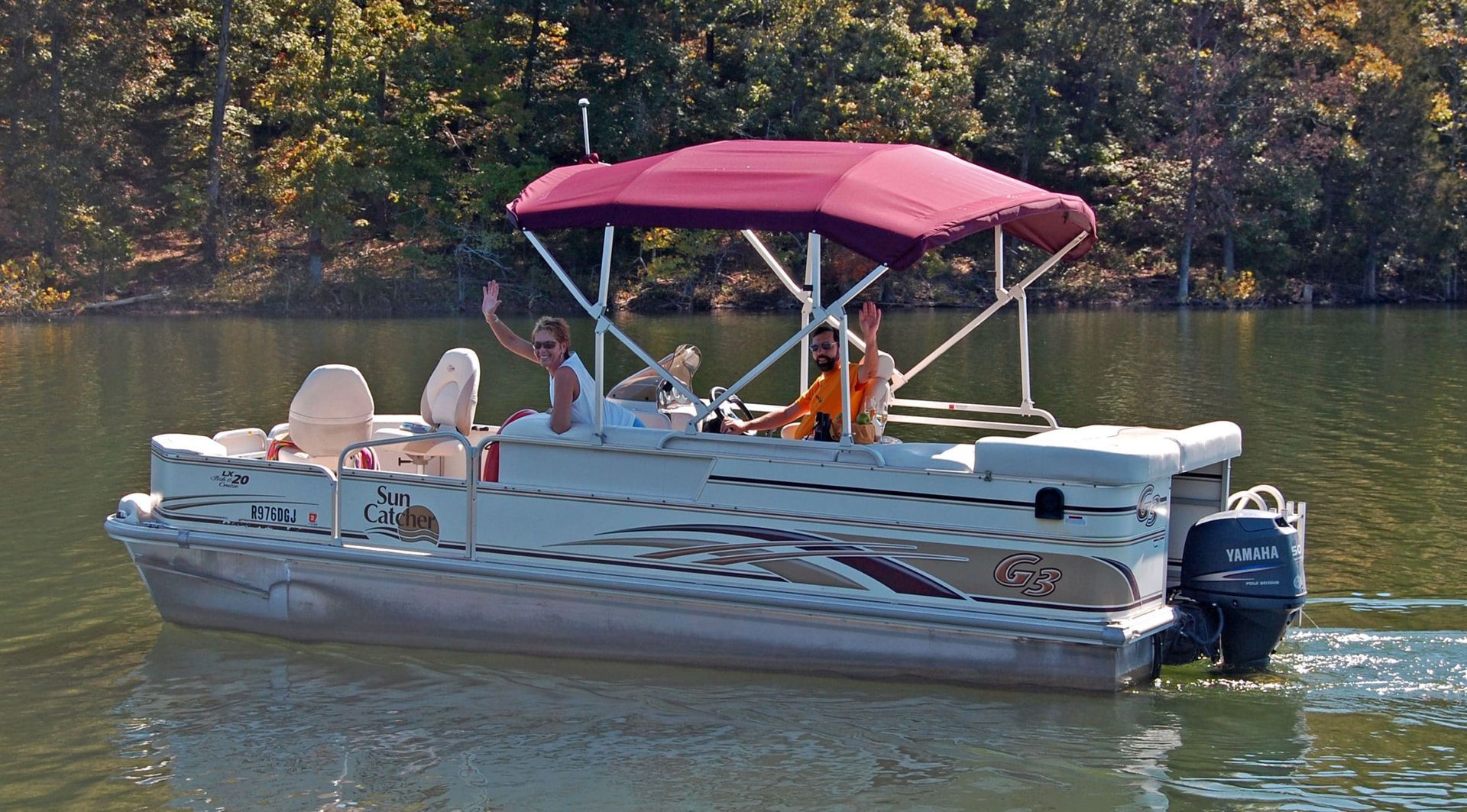 A pontoon boat with a red canopy is floating on a lake.