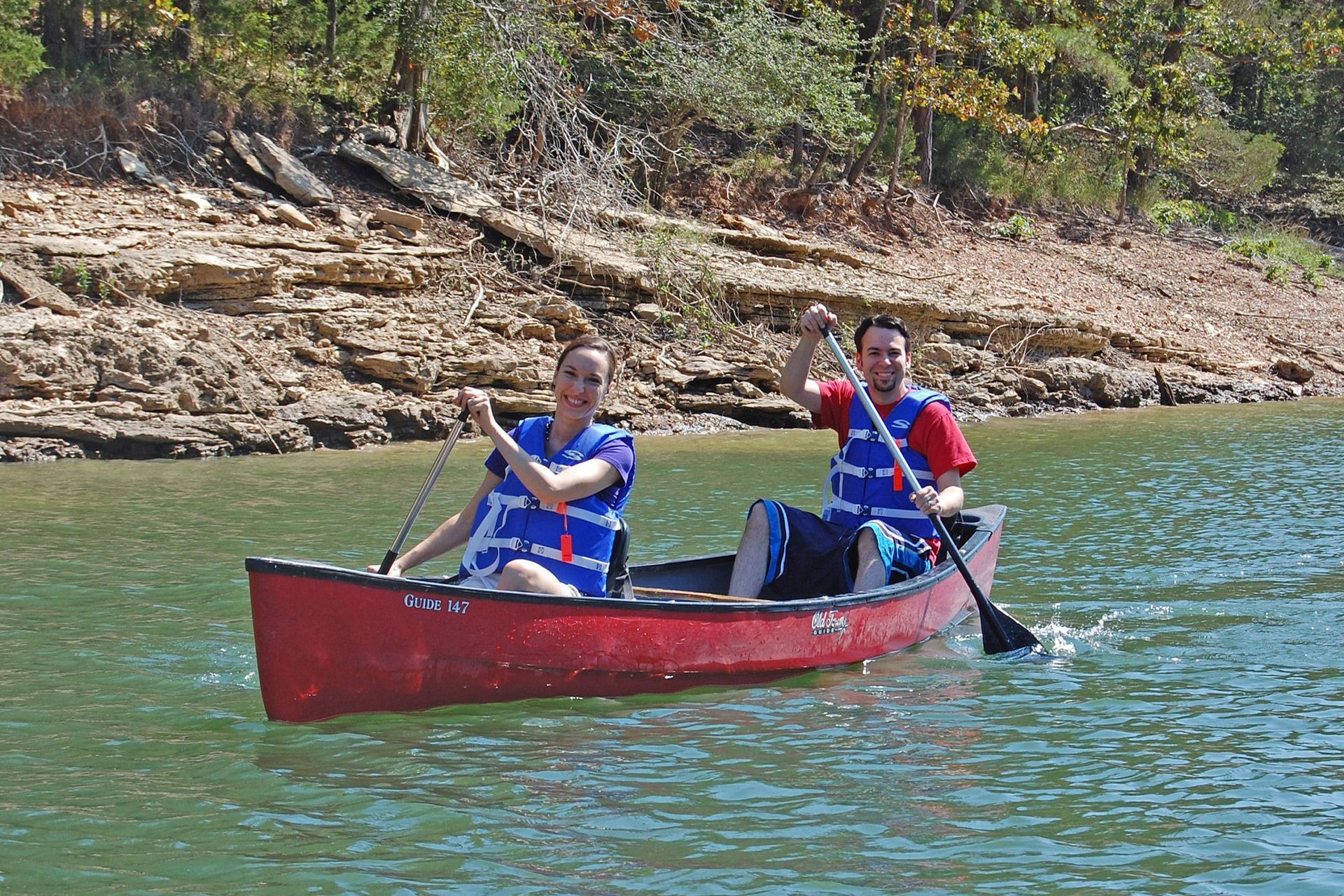 Two people are paddling a red canoe on a lake.