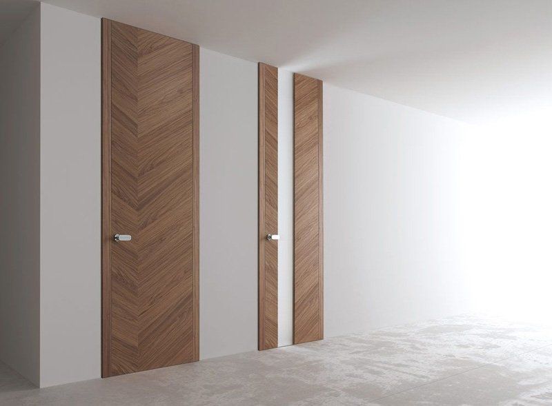 Corridoio minimalista con tre porte a pannelli in legno e pareti bianche su un pavimento chiaro.