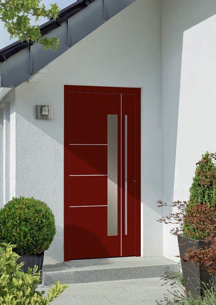 Porta d'ingresso rossa con lunghe maniglie argentate su un moderno ingresso di una casa bianca.
