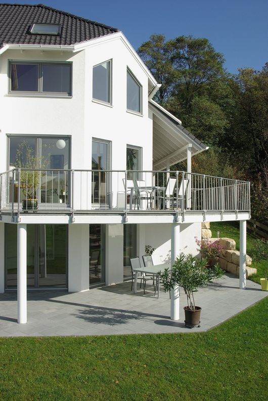 Casa moderna bianca con terrazza rialzata e patio su un prato verde.