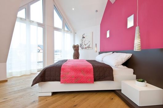 Luminosa camera da letto moderna con una parete d'accento rosa, ampie finestre e un letto ben rifatto con un cane seduto sopra.