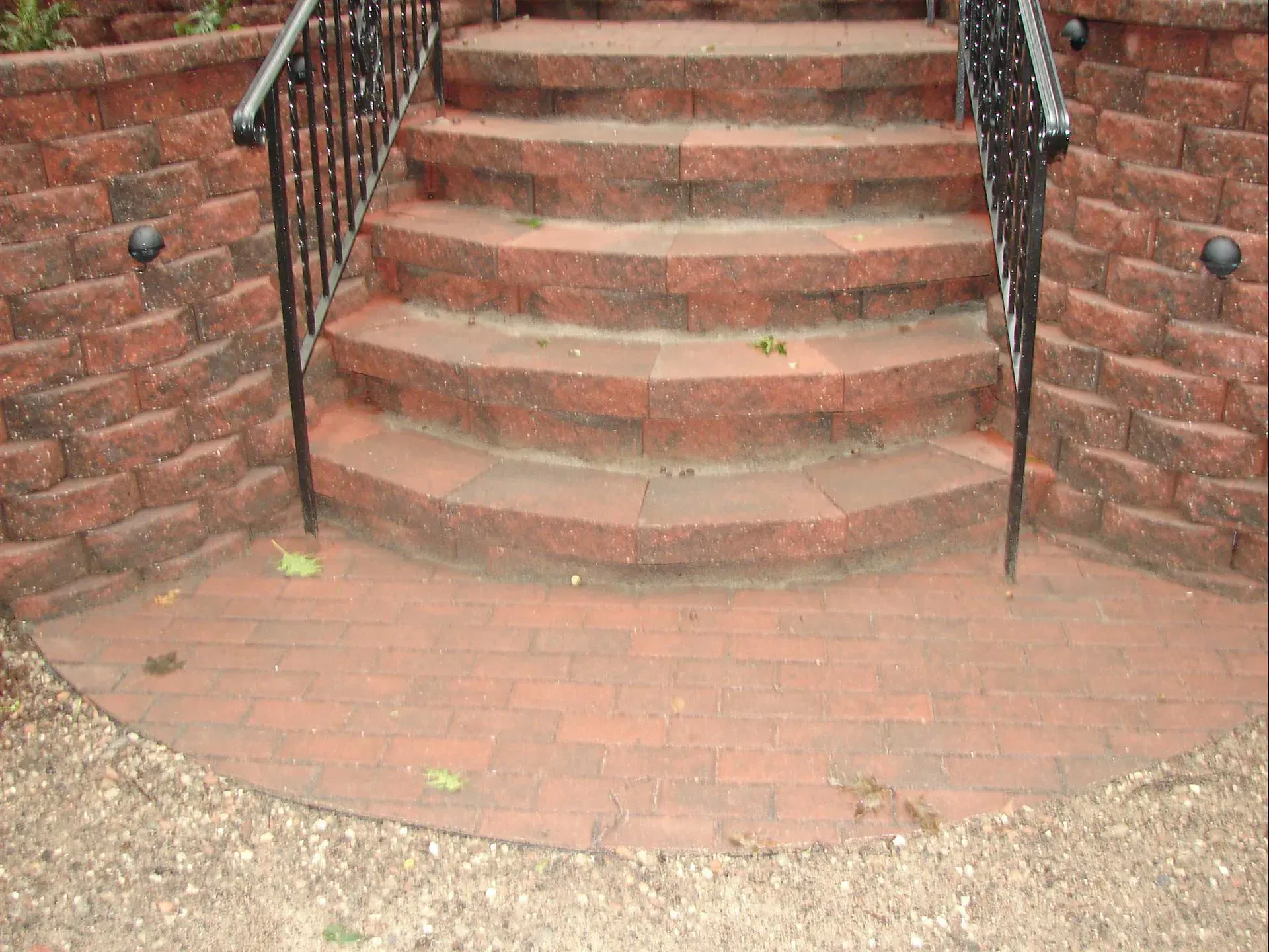 Brick steps leading up to a doorway, flanked by brick walls and black metal railings.
