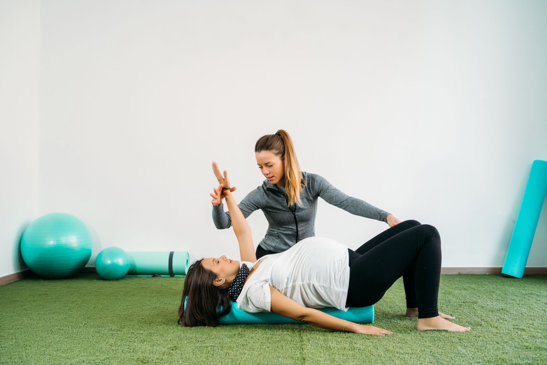 Pregnant woman doing exercises with a trainer in a gym on a green mat.